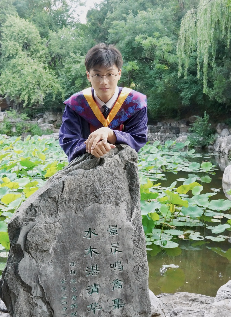 Hengrui Wang in doctoral graduation robes by the pond at Tsinghua University